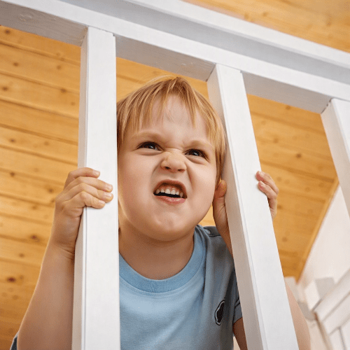 barriere-pour-enfant-garcon-grimace-entre-barreaux-bois-rambarde-interieure-gardien-calme